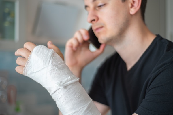 Man with a bandaged arm talking on the phone, looking concerned.