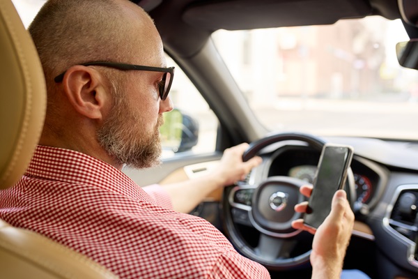 Man driving a car while holding and looking at a smartphone in his right hand.